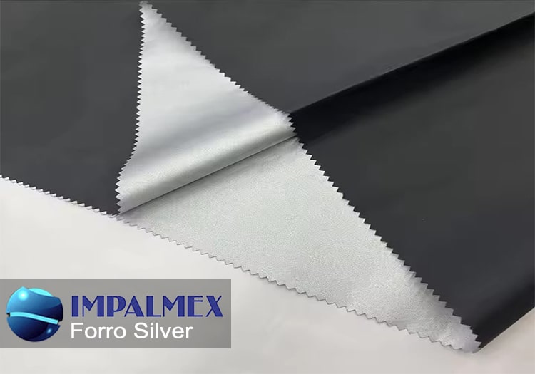 Un primer plano de la tela Forro Silver, destacando su superficie plateada y su textura impermeable, enrollada parcialmente en un rollo